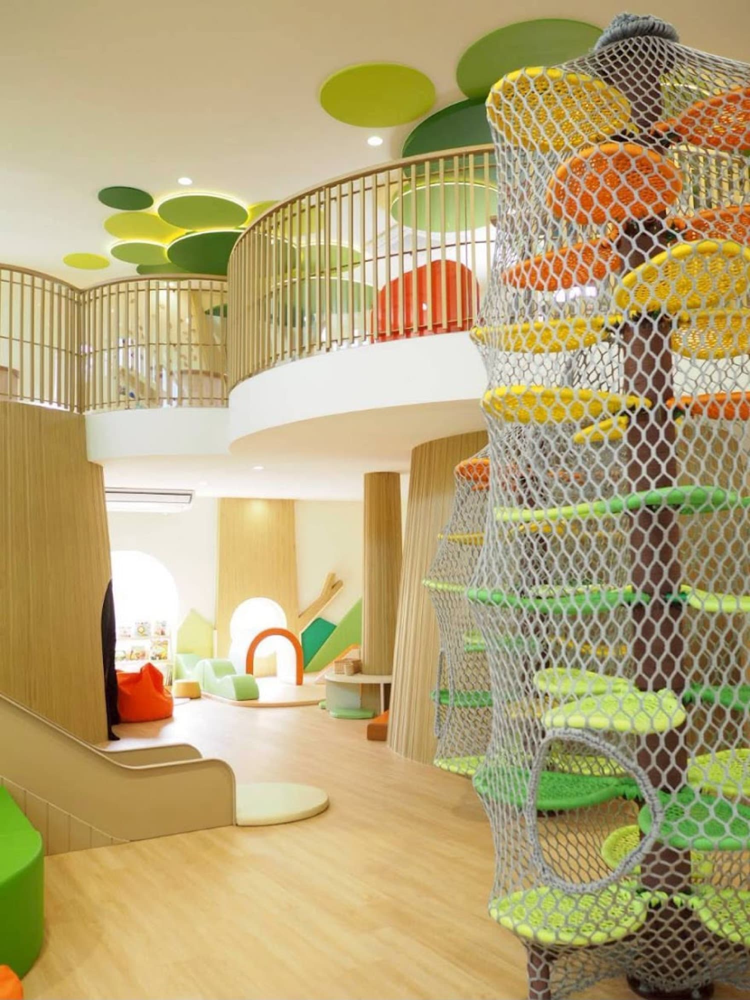 The bright, open two-floor play space at Forest Tales in Bangkok, with a tall netted climbing tower and green lily-pad discs across the ceiling