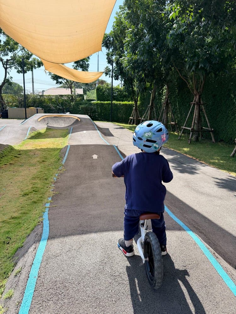 Toddler in a blue helmet on a balance bike, riding the track at Seven Sisters Cafe in Bangkok