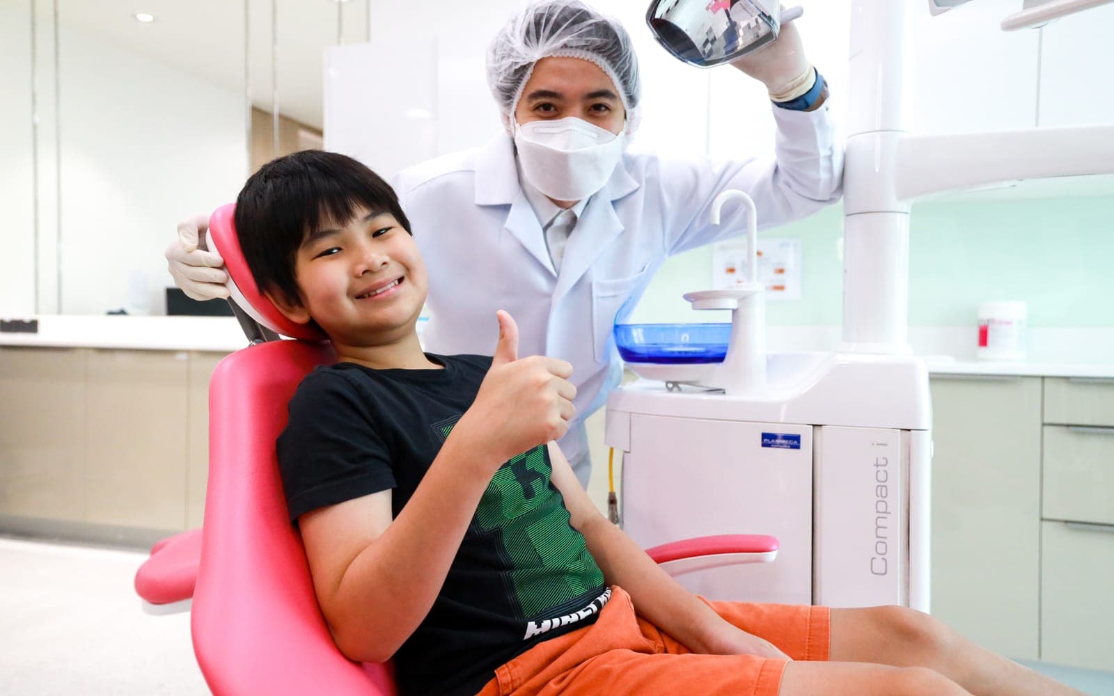 A young patient giving a thumbs up from the dental chair beside his dentist at Bangkok International Dental Hospital, Bangkok
