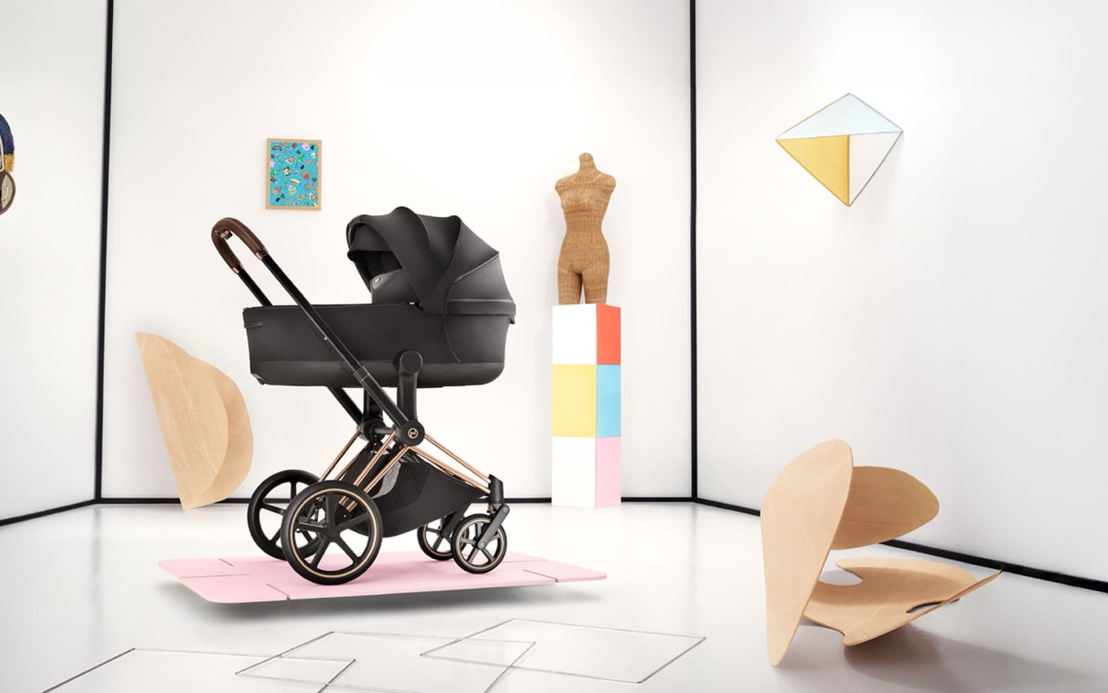 A black Cybex Priam stroller with a rose gold frame on a soft pink platform in a bright, minimal room
