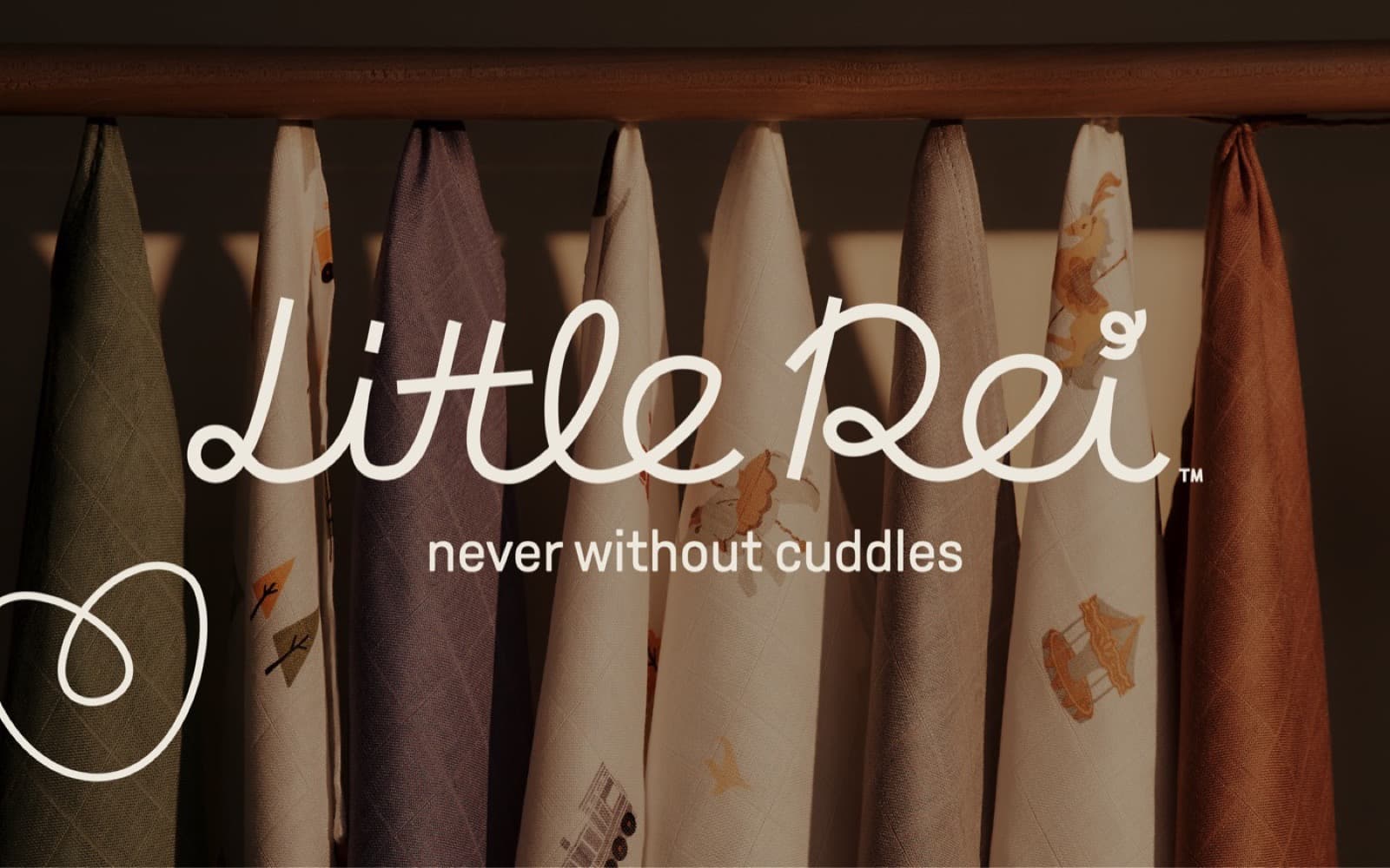 Little Rei bamboo swaddle blankets in green, lilac, cream and rust hanging from a wooden rail