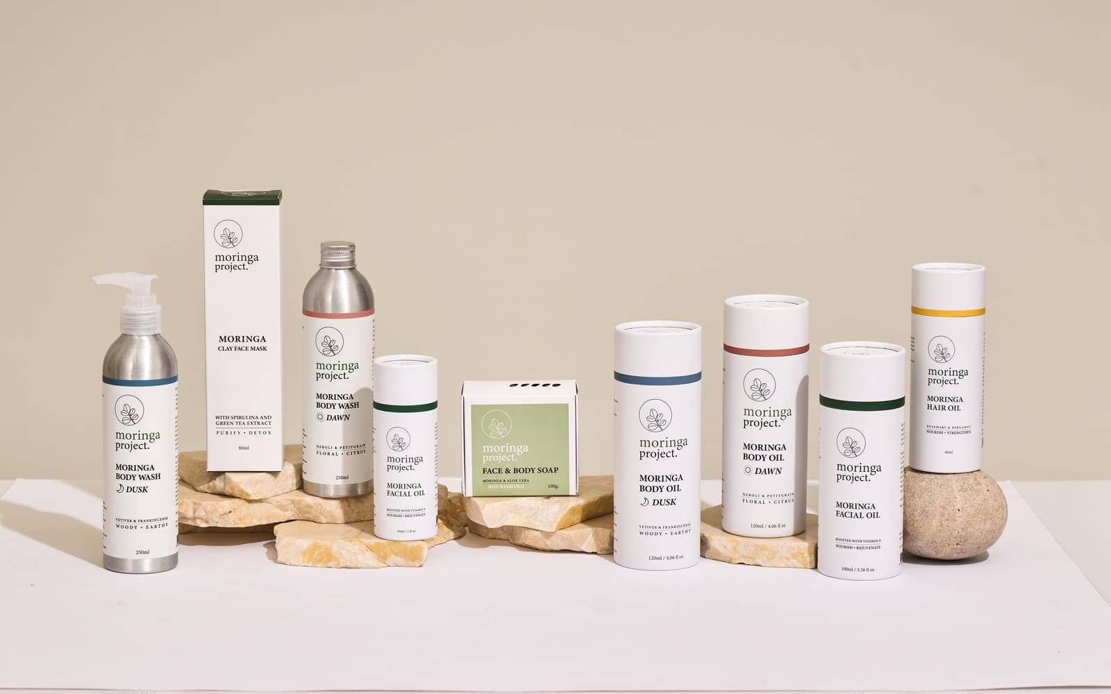 The Moringa Project skincare range on stone props: body wash, clay face mask, facial oil, soap, body oil, and hair oil