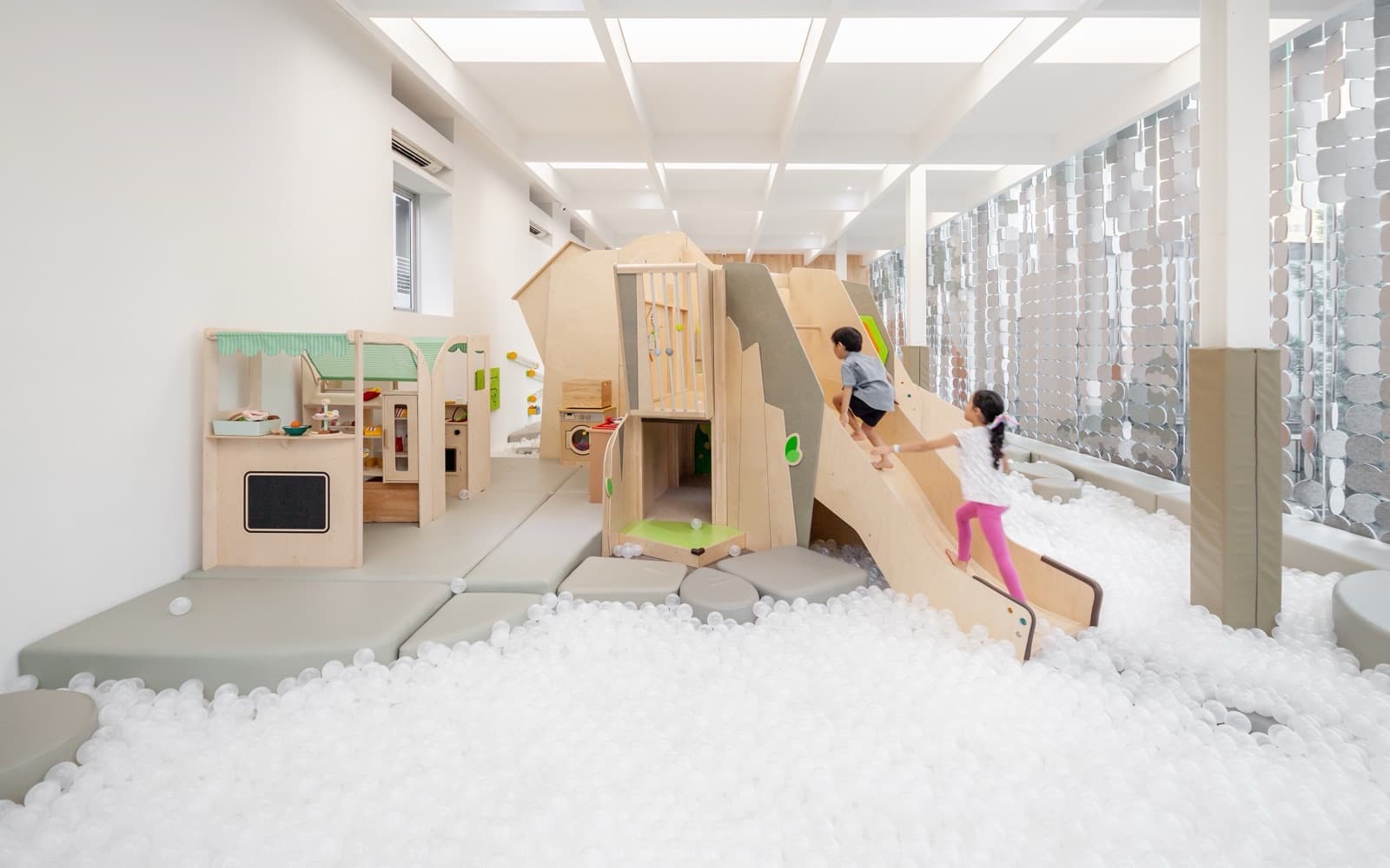 Two children climbing the wooden slide out of the white ball pit at Playville